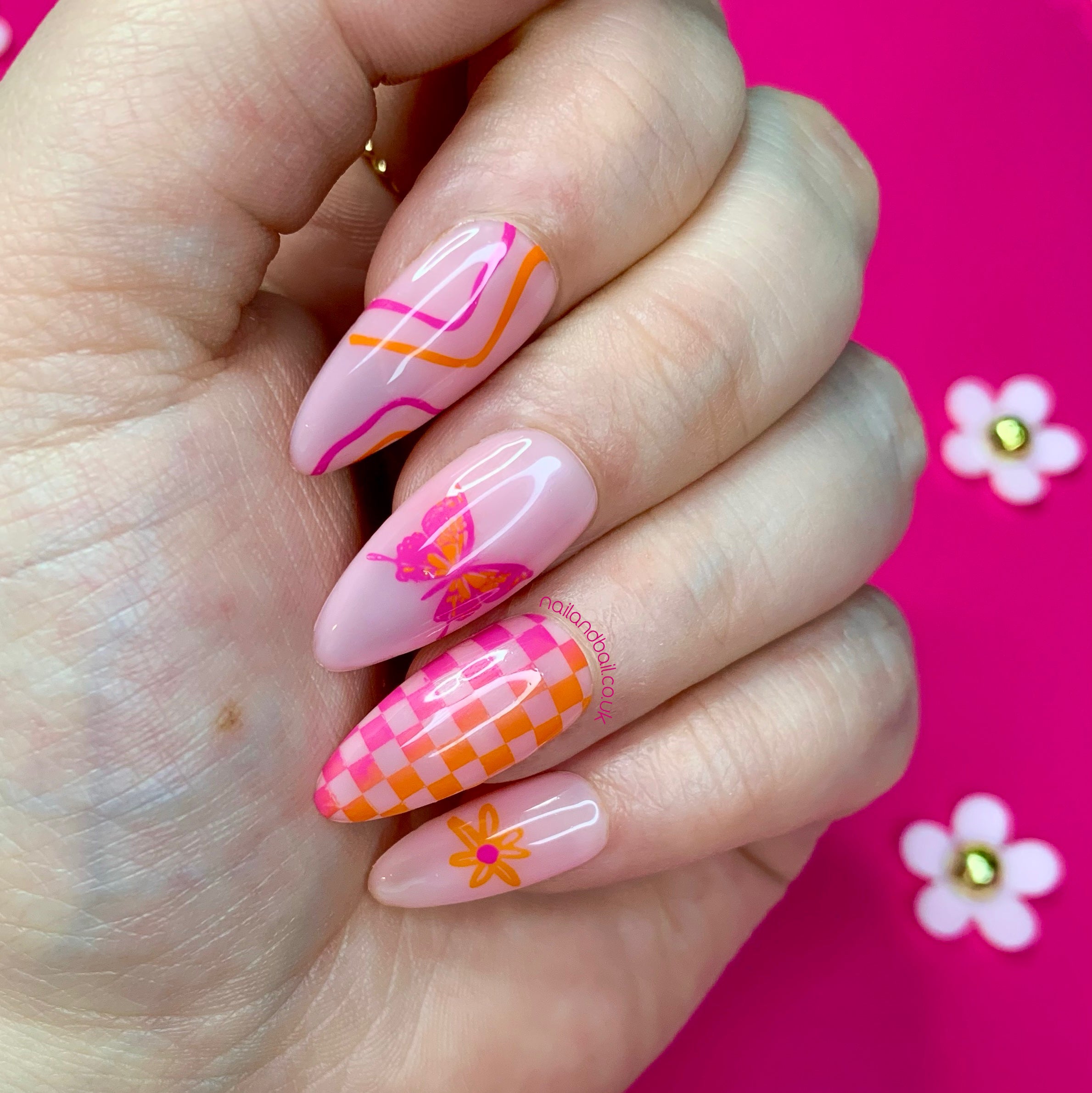 Pink nude press-on nails with orange and pink butterflies, checkered nail art, floral details, and retro swirl designs