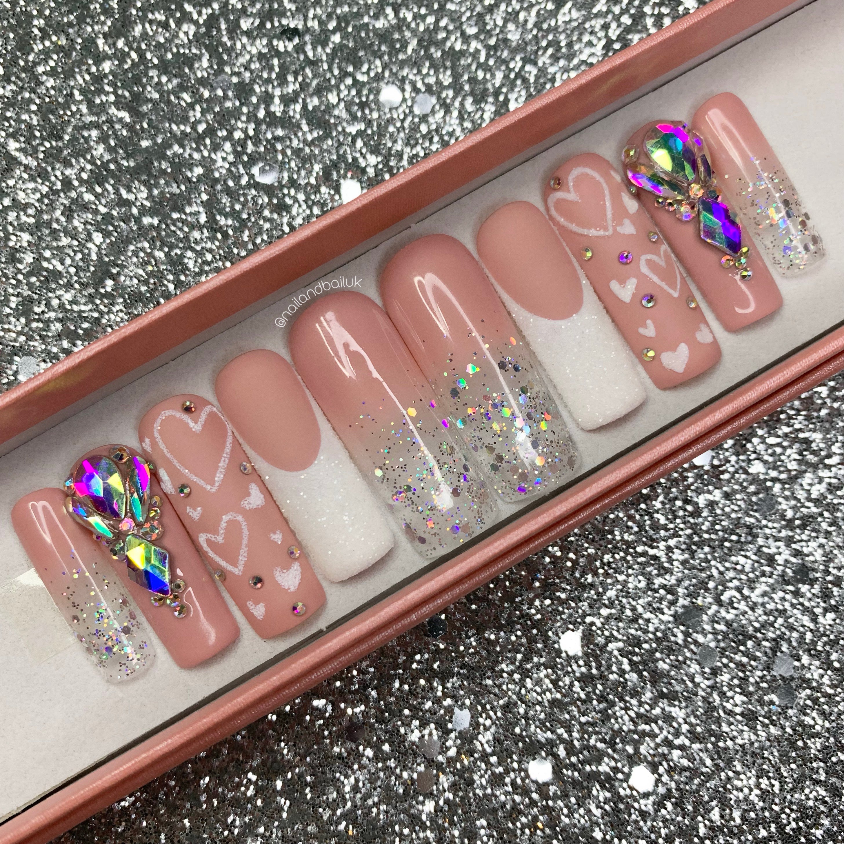 Nude ombre press-on nails with holographic glitter, sugared French tips, crystal clusters, and heart nail art
