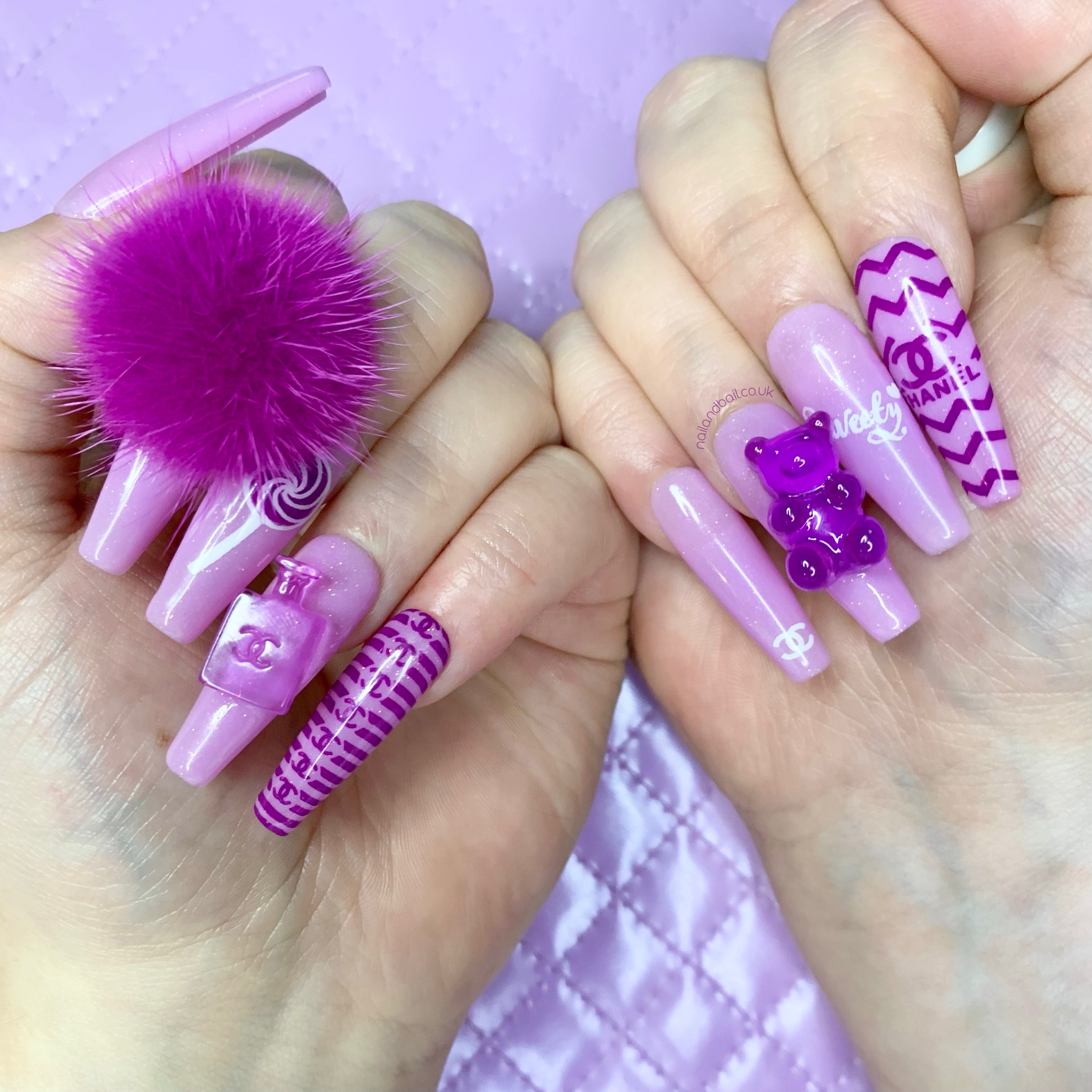 Purple glitter press-on nails with luxury-inspired artwork, gummy charms, perfume bottle charm, and fluffy pom-pom