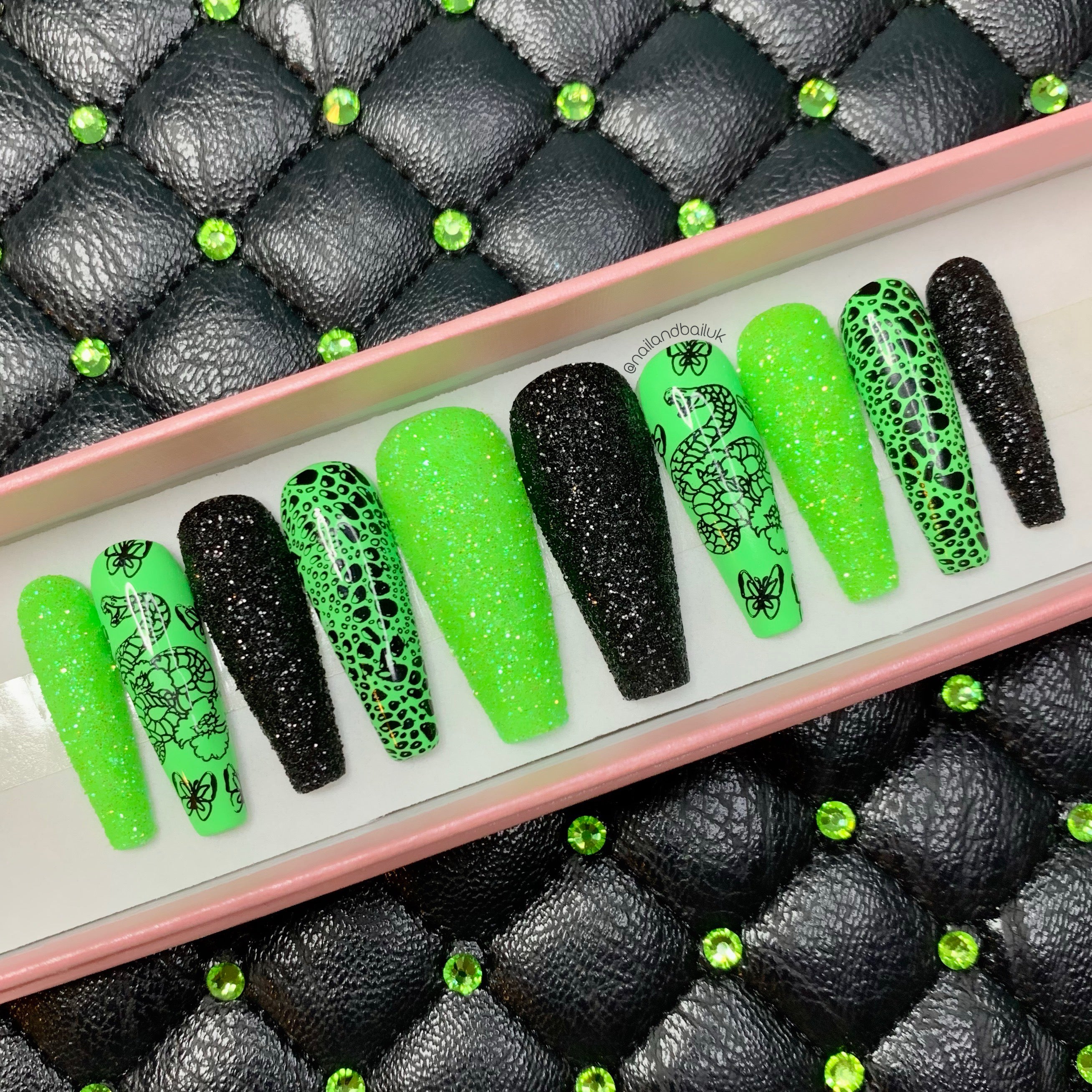 Green and black press-on nails with snake artwork, butterfly details, and sugared glitter finish