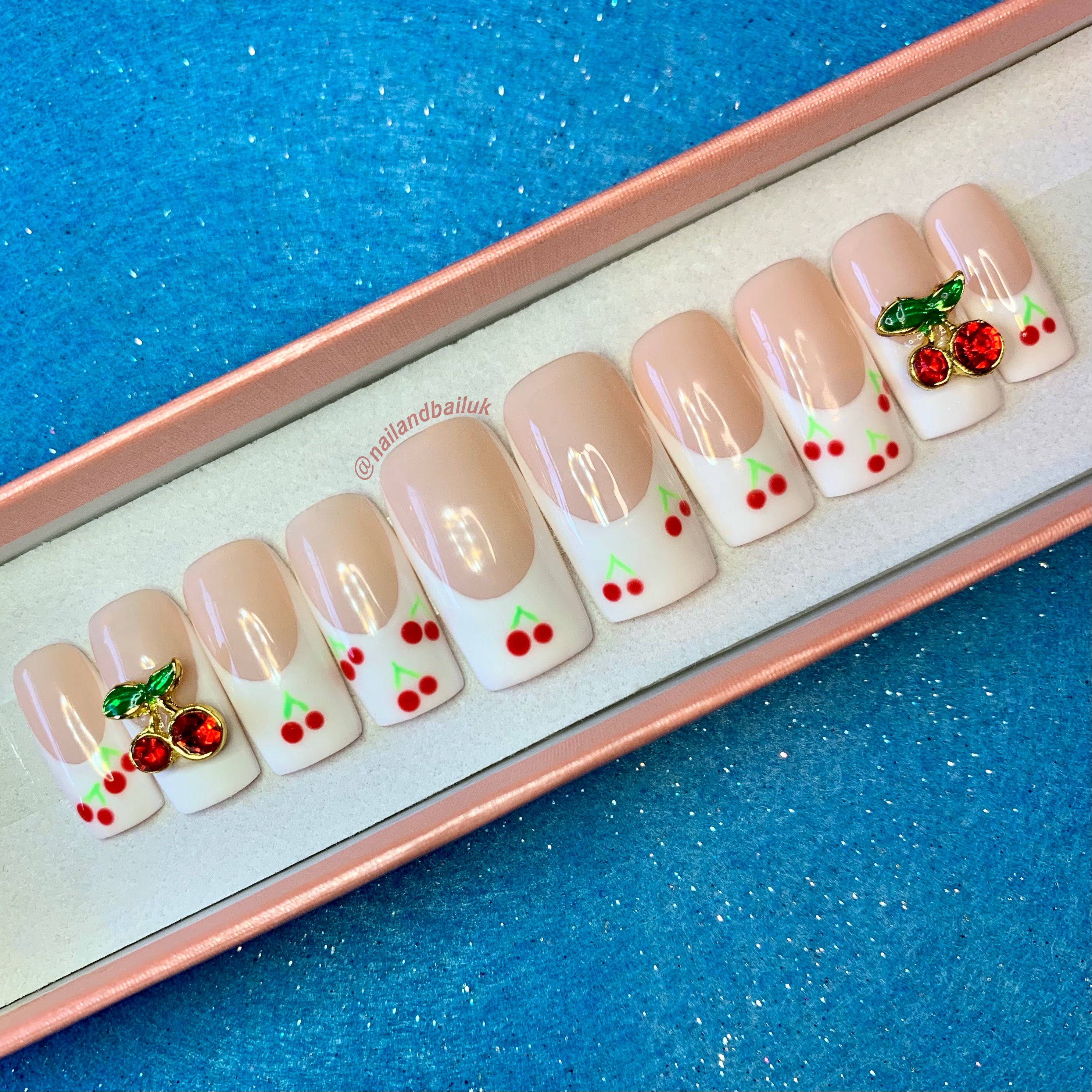 Very Cherry press-on nails – hand-painted white French tips with cherries, cherry embellishments, and a glossy top coat. Sweet, playful, and stylish!