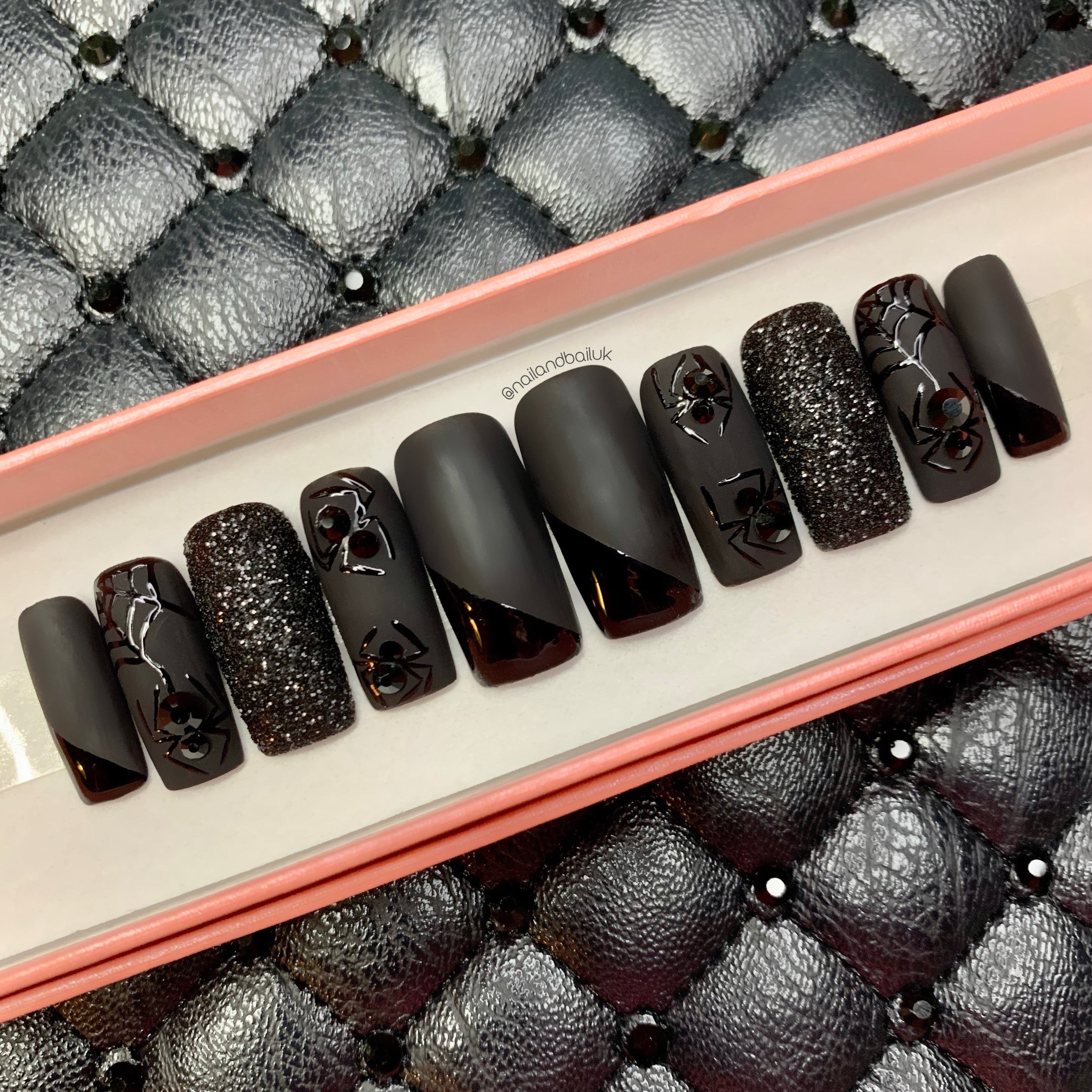 Matte black press-on nails with crystal spiders, glossy spiderwebs, and black sugared glitter details